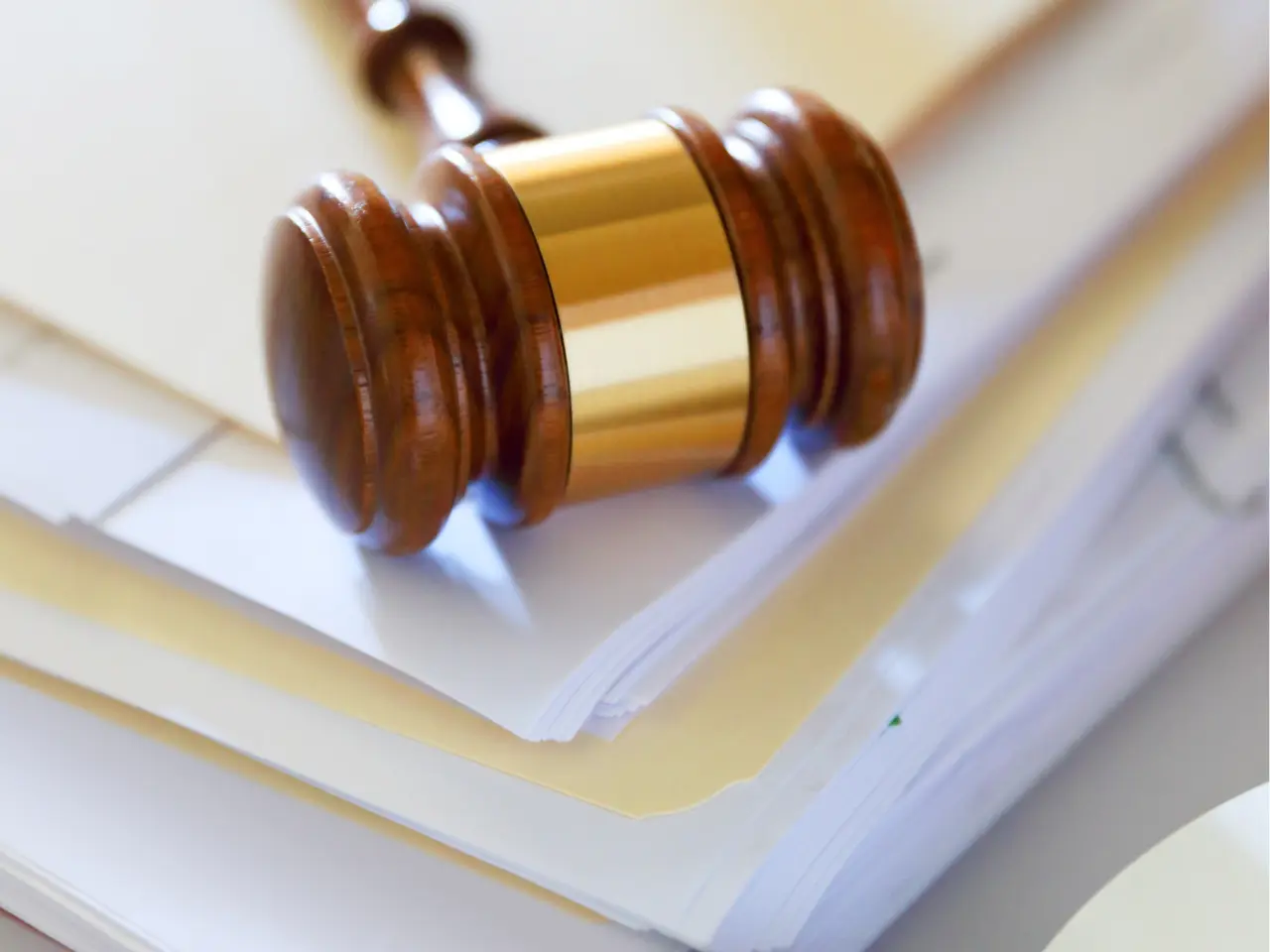 A wooden judge’s gavel rests on top of a stack of white papers and file folders, symbolizing legal proceedings or judicial decisions.