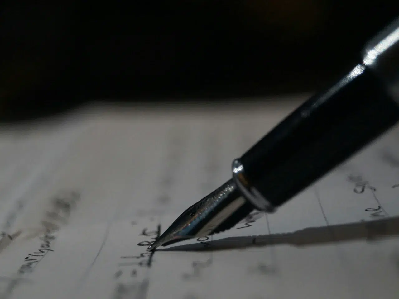 A close-up of a fountain pen writing on lined paper, with handwritten text slightly blurred in the background.