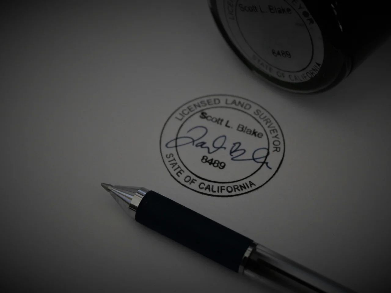 A pen lies on paper displaying an official stamp and signature for a licensed land surveyor in California.