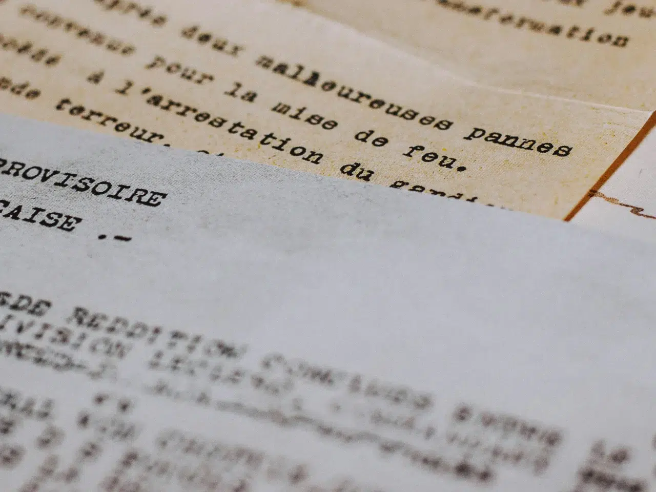 Close-up of vintage typewritten French documents layered on top of each other, featuring visible text and slightly yellowed paper edges.