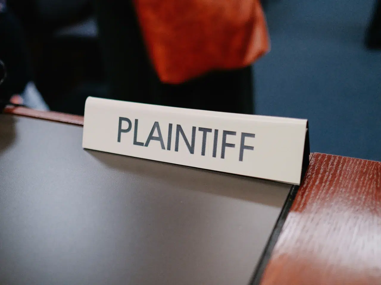 A desk sign labeled PLAINTIFF sits on a courtroom table, indicating the party who initiates a lawsuit.