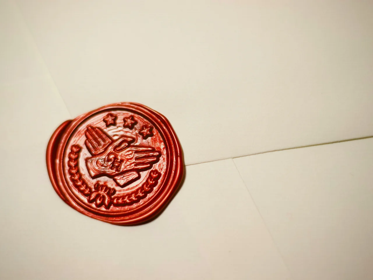 A red wax seal with an embossed bird and star design is stamped on a cream-colored envelope.