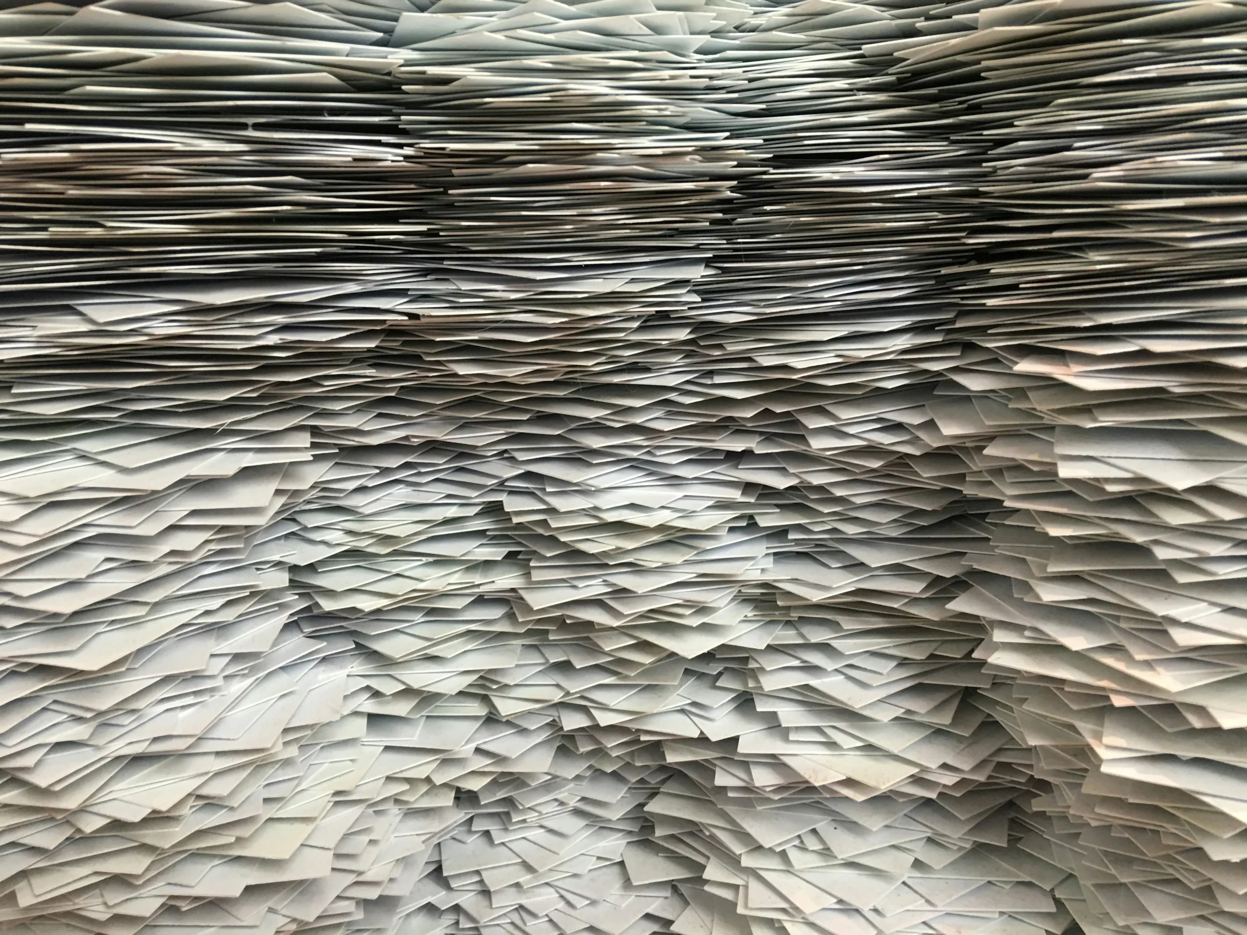 A large, dense stack of overlapping paper sheets arranged in uneven horizontal layers, creating a textured and chaotic appearance.