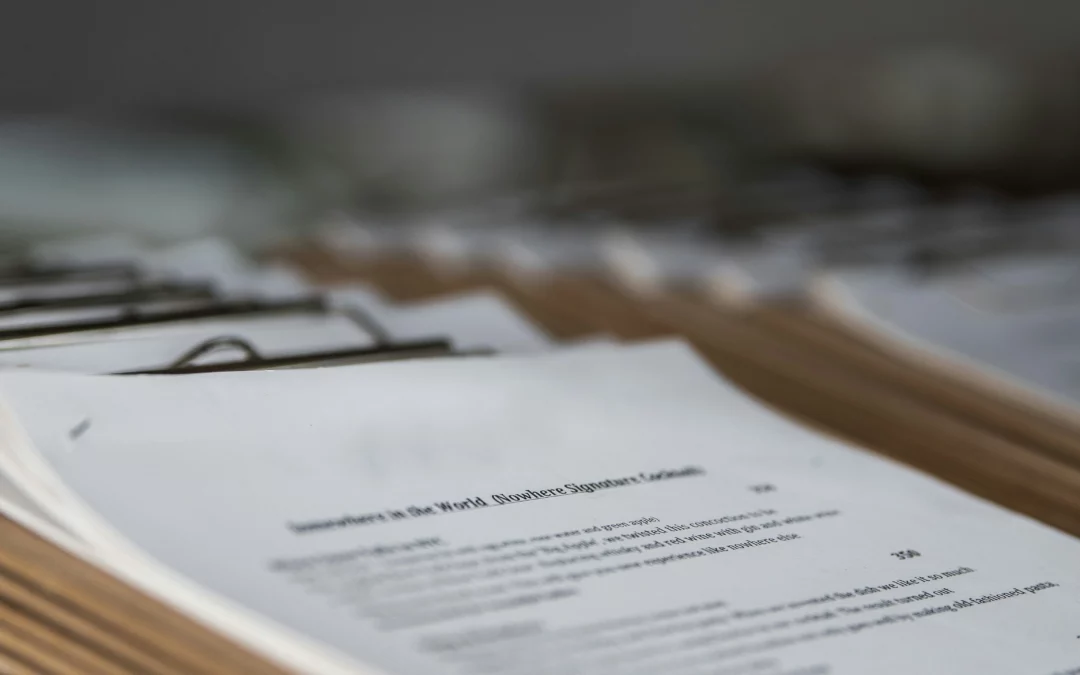 A close-up of several stacks of printed documents clipped to brown folders, with text visible on the top page, arranged in a row on a table.