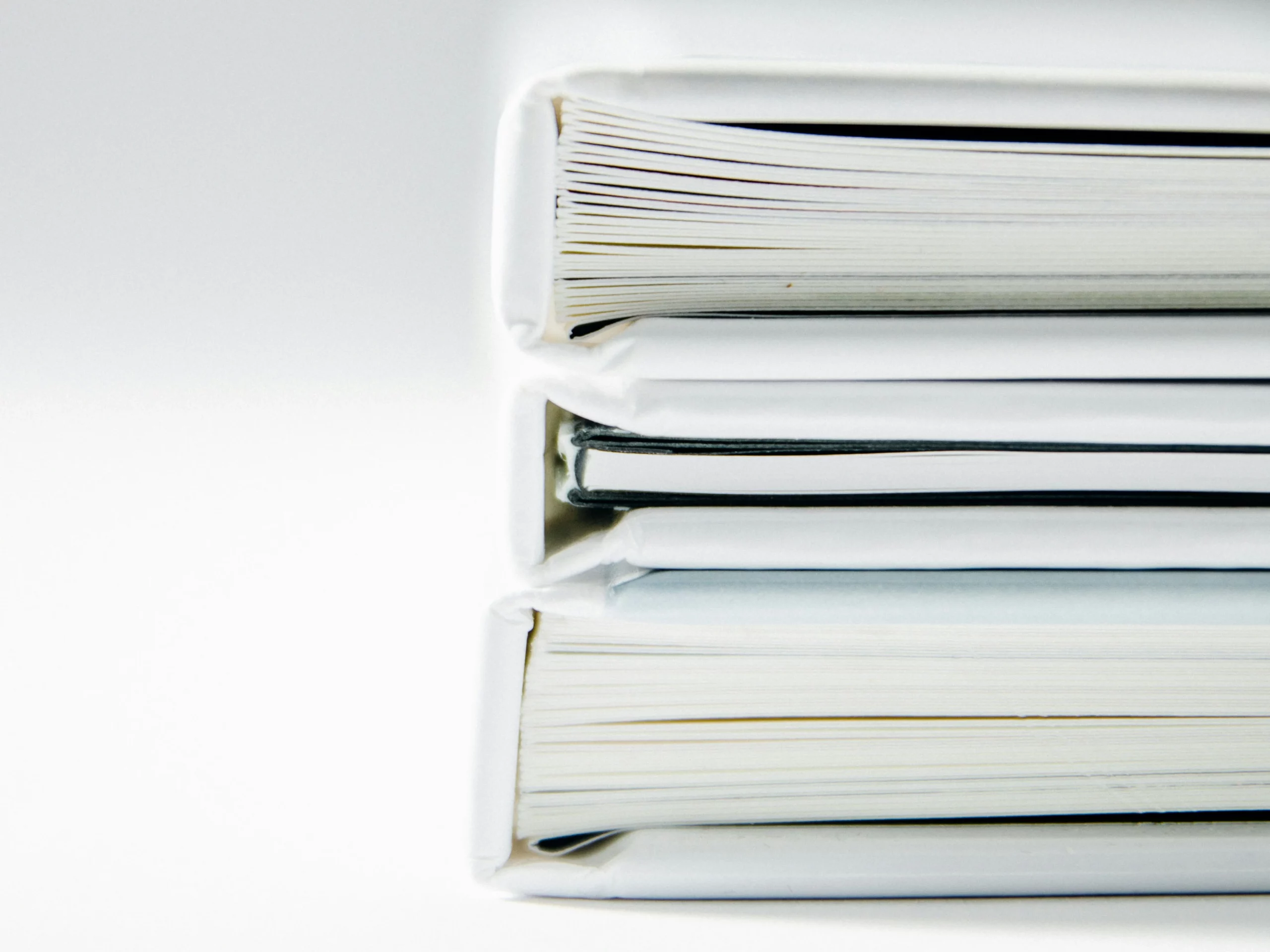 Close-up of the spines of three stacked white books or binders, showing the edges of their pages against a plain white background.