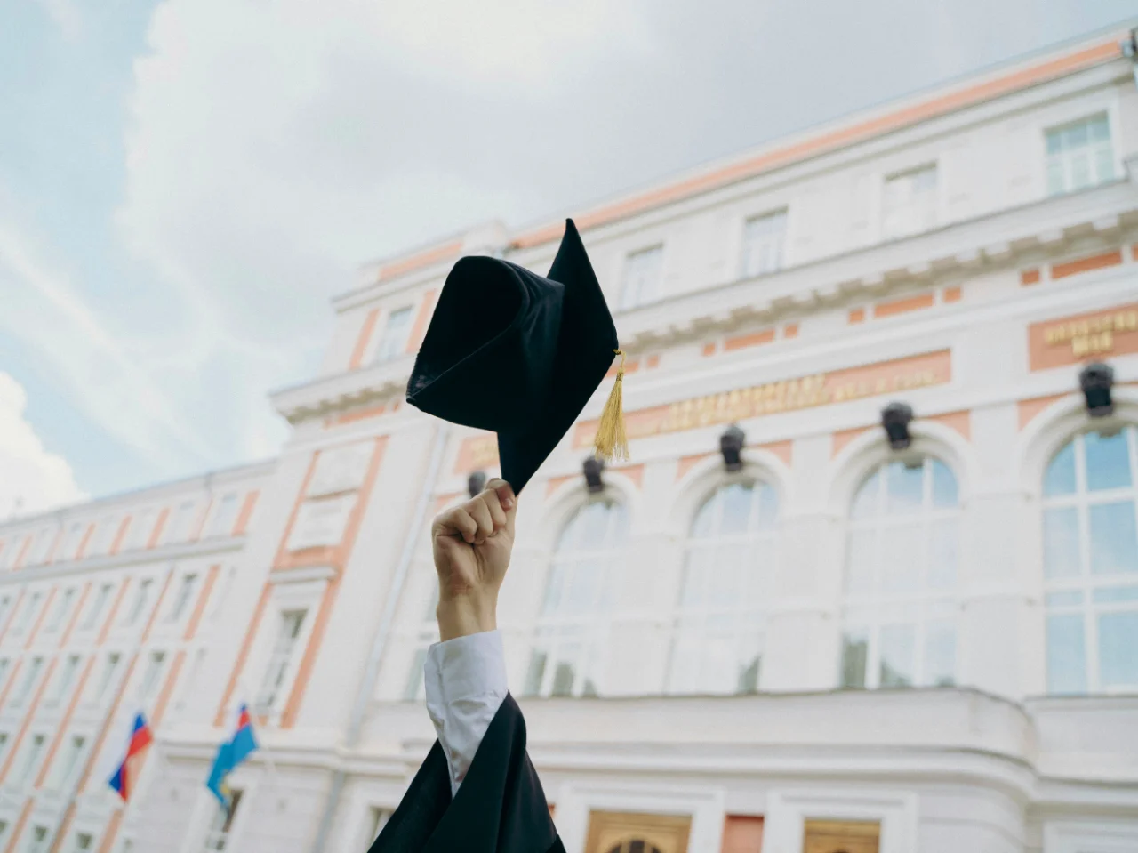 A graduation cap held up in front of a university building